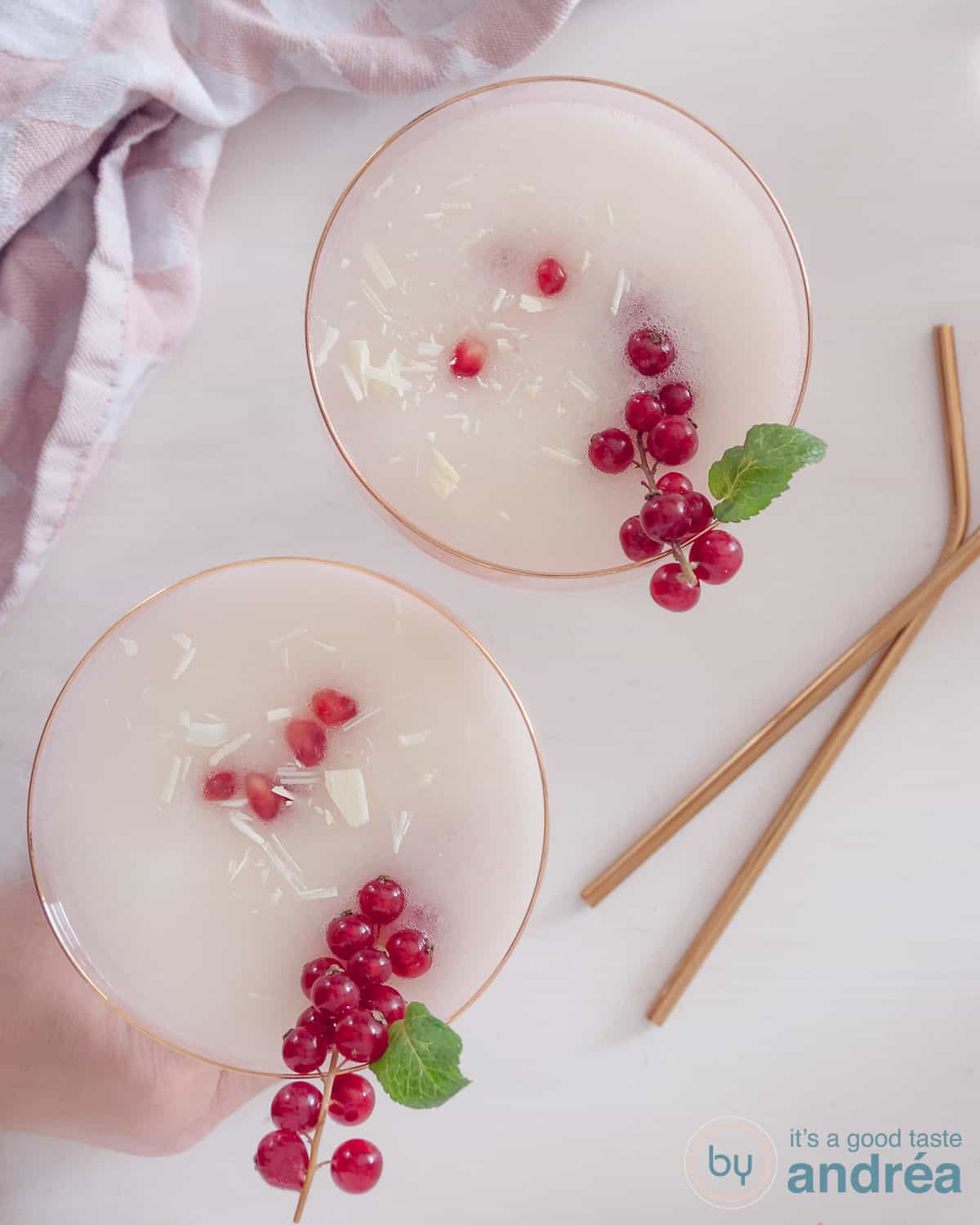 Een foto van bovenaf van een witte ondergrond met twee champagneglazen gevuld met scroppino zonder alcohol en met citroenijs. Twee gouden rietjes liggen aan de rechterzijde ernaast.