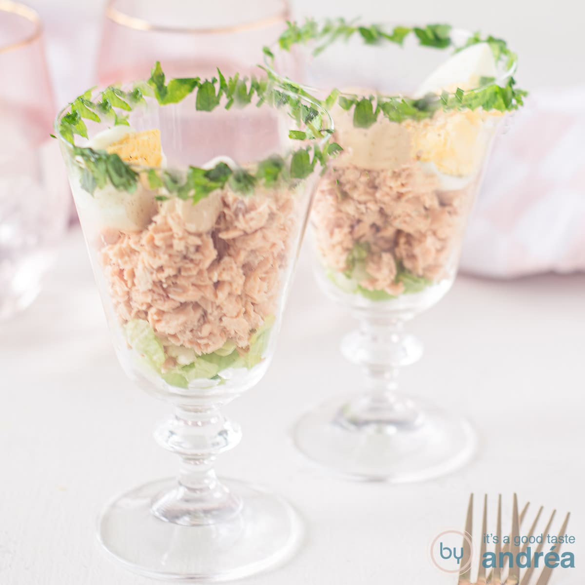 Een vierkante foto met twee cocktailglazen gevuld met zalm, whiskysaus en een eitje. Bovenin is de rand van het glas gegarneerd met peterselie.