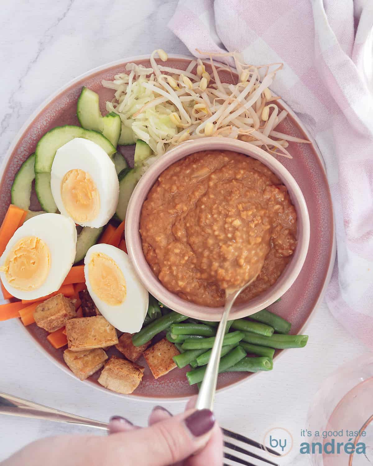 Een foto van bovenaf van een roze bord met boontjes, tofu, wortels, komkommer en tauge met eieren: gadogado met satésaus