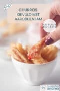 Een wit bakje met aardbeienchurro's waaruit een hand er een pakt. Een tekst bovenin Churros gevuld met aardbeienjam, makkelijk recept