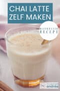 Een glas gevuld met chai tea latte met een gouden lepel. Een tekst: chai latte zelf maken, makkelijk recept