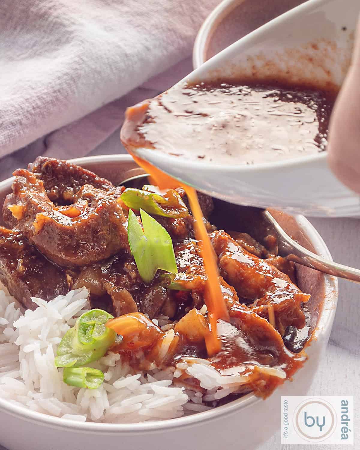 Een hoogtefoto met een kom met babi pangang, rijst en wat lente-ui. Babi pangangsaus wordt in de kom gegoten.
