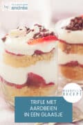 Een glaasje gevuld met verse aardbeien, cake en room, een tweede glas er schuin achter. Een tekst: trifle met aardbeien in een glaasje, makkelijk recept