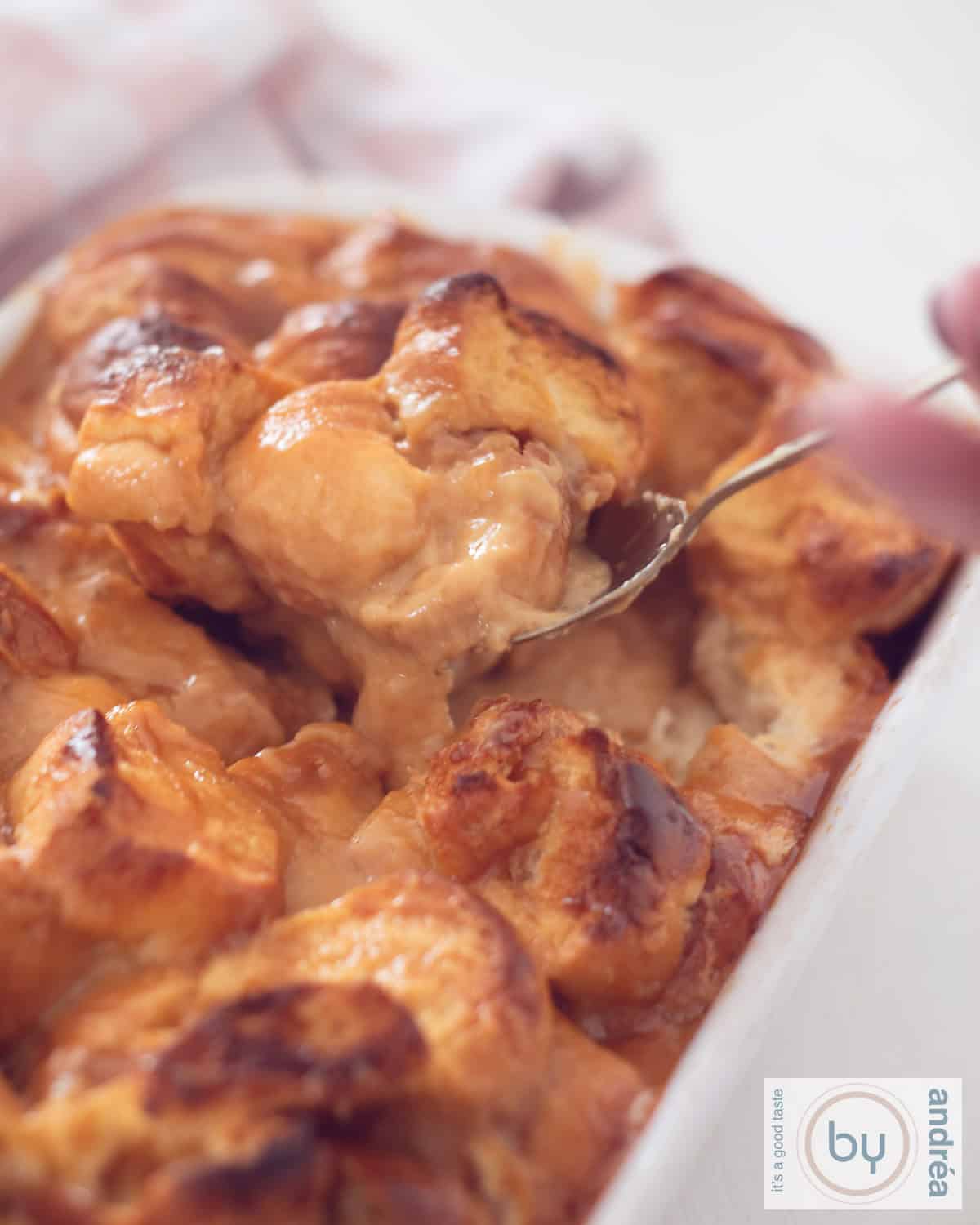 Een hoogtefoto met een ovenschaal gevuld met brioche en zoete karamelsaus. Een lepel pakt een schep