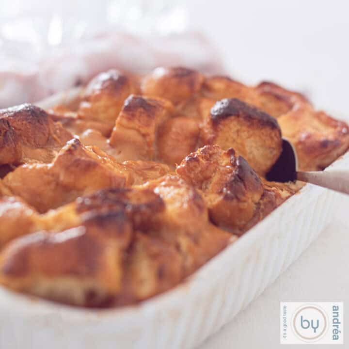 Een vierkante foto met een broodpudding met Dulce de Leche en brioche. Een lepel neemt een schep