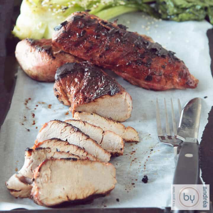 Een vierkante foto met twee Char Siu, waarvan 1 in reepjes gesneden op een bakpapier
