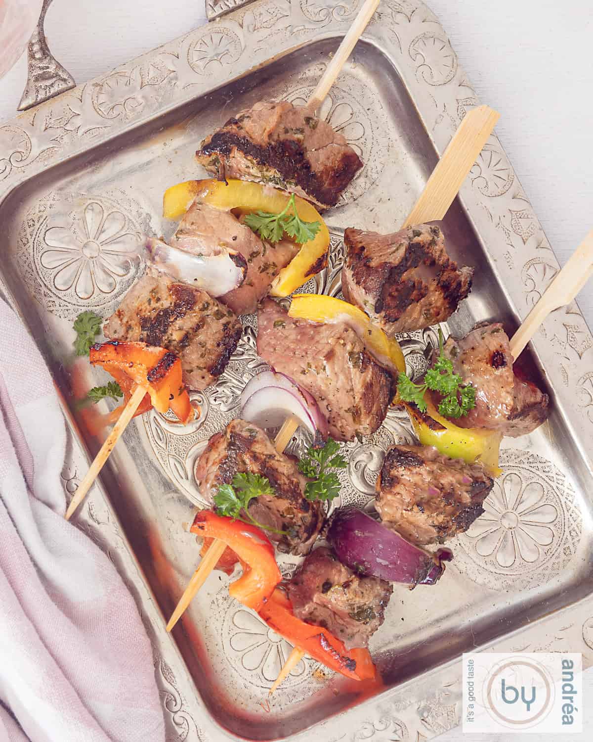 Een foto van bovenaf van een zilveren schaal met drie biefstuk kebabs met paprika en ui.