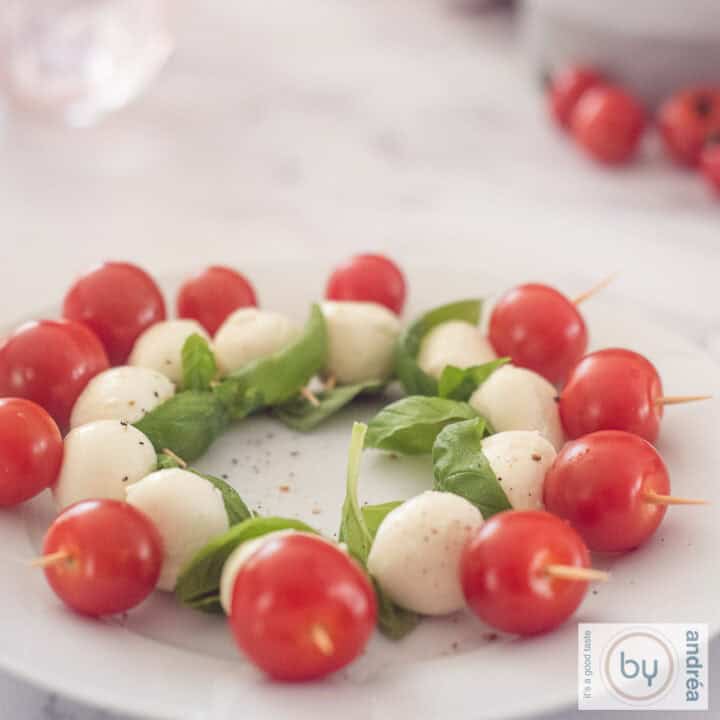 Een vierkante foto met een schaal gevuld met mini Caprese stokjes met cherry tomaten, mozzarella en baslicum blaadjes.