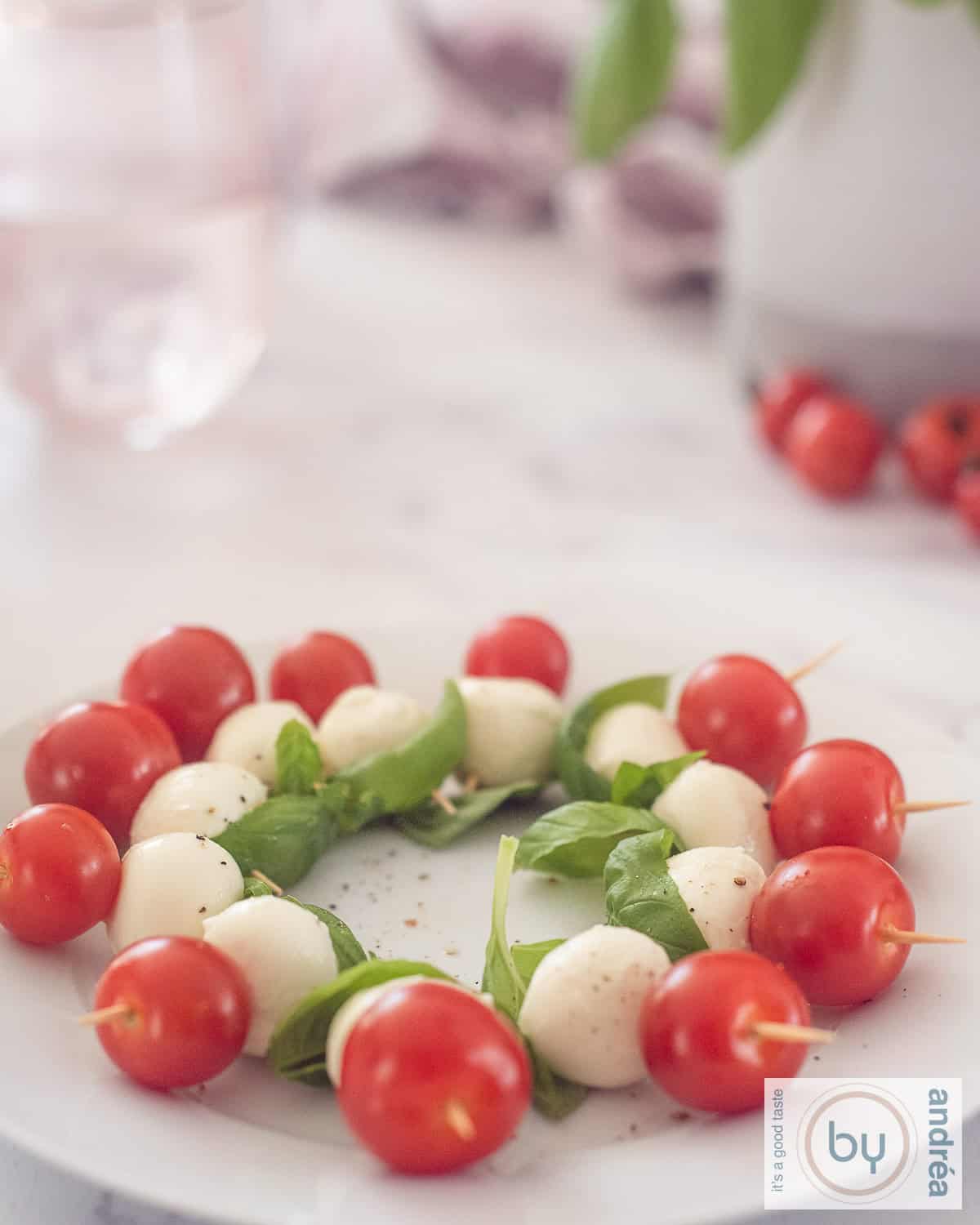 Een hoogtefoto met een wit bord gevuld met caprese hapjes met tomaat, mozzarella en baslicum.