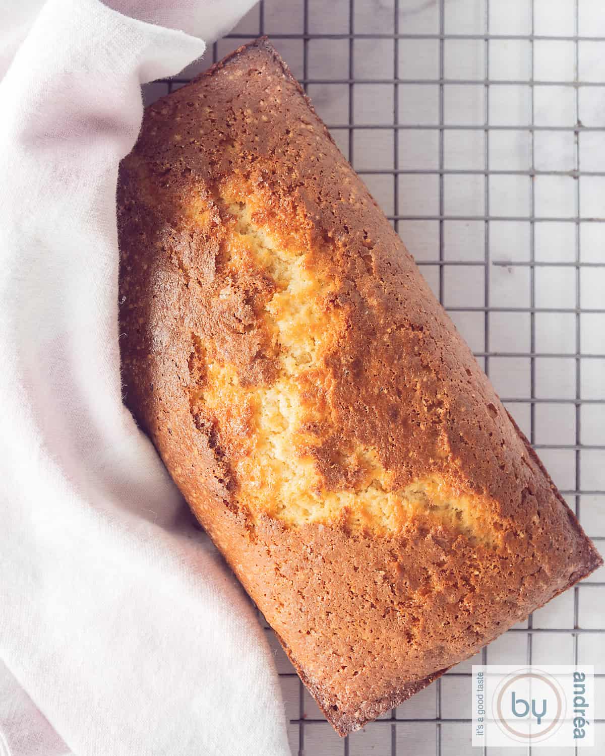 Een foto van bovenaf van een appelmoescake op een rek. Een roze witte theedoek ligt op een deel van de cake.