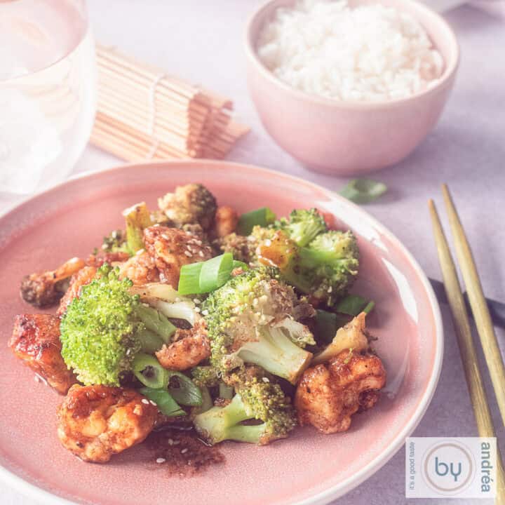 Een vierkante foto met een roze bord gevuld met broccoli, kip en hoisinsaus. Een kom rijst in de achtergrond.