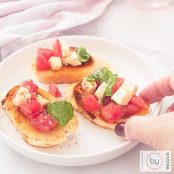 Een vierkante foto met een rond wit bord met drie bruschettes met tomaat, mozzarella en basilicum topping