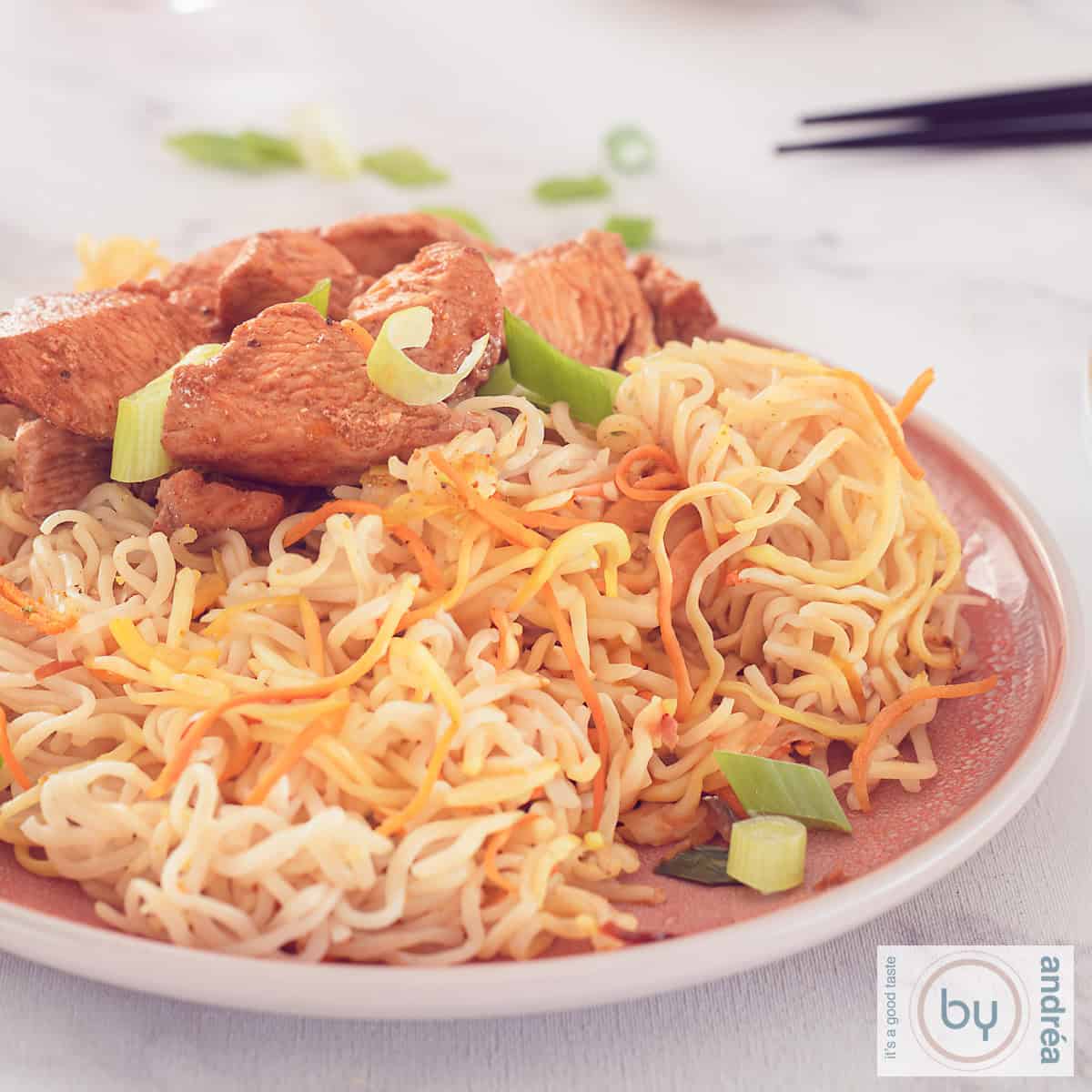 Een vierkante foto met een roze bord met mie en kantonese kip. Een witte ondergrond.