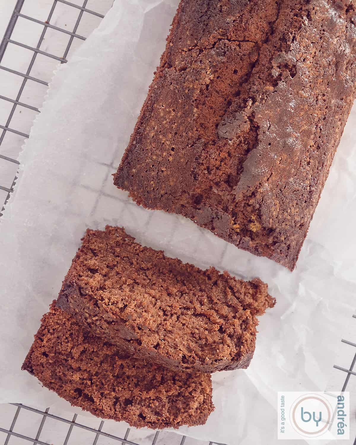 Een foto van bovenaf van een rek met bakpapier met een chocolade cake met cacao waar twee plakjes afgesneden zijn.