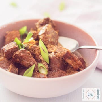 Een vierkante foto van een roze schaal met stoofvlees: Daging Sapi Roedjak uit Indonesië gemaakt in de slowcooker. Een witte ondergrond.
