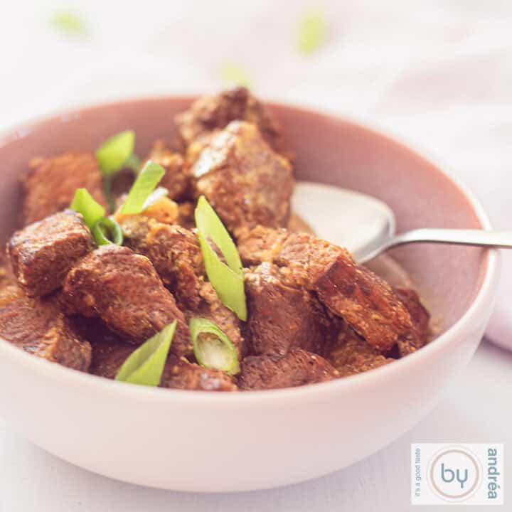 Een vierkante foto van een roze schaal met stoofvlees: Daging Sapi Roedjak uit Indonesië gemaakt in de slowcooker. Een witte ondergrond.