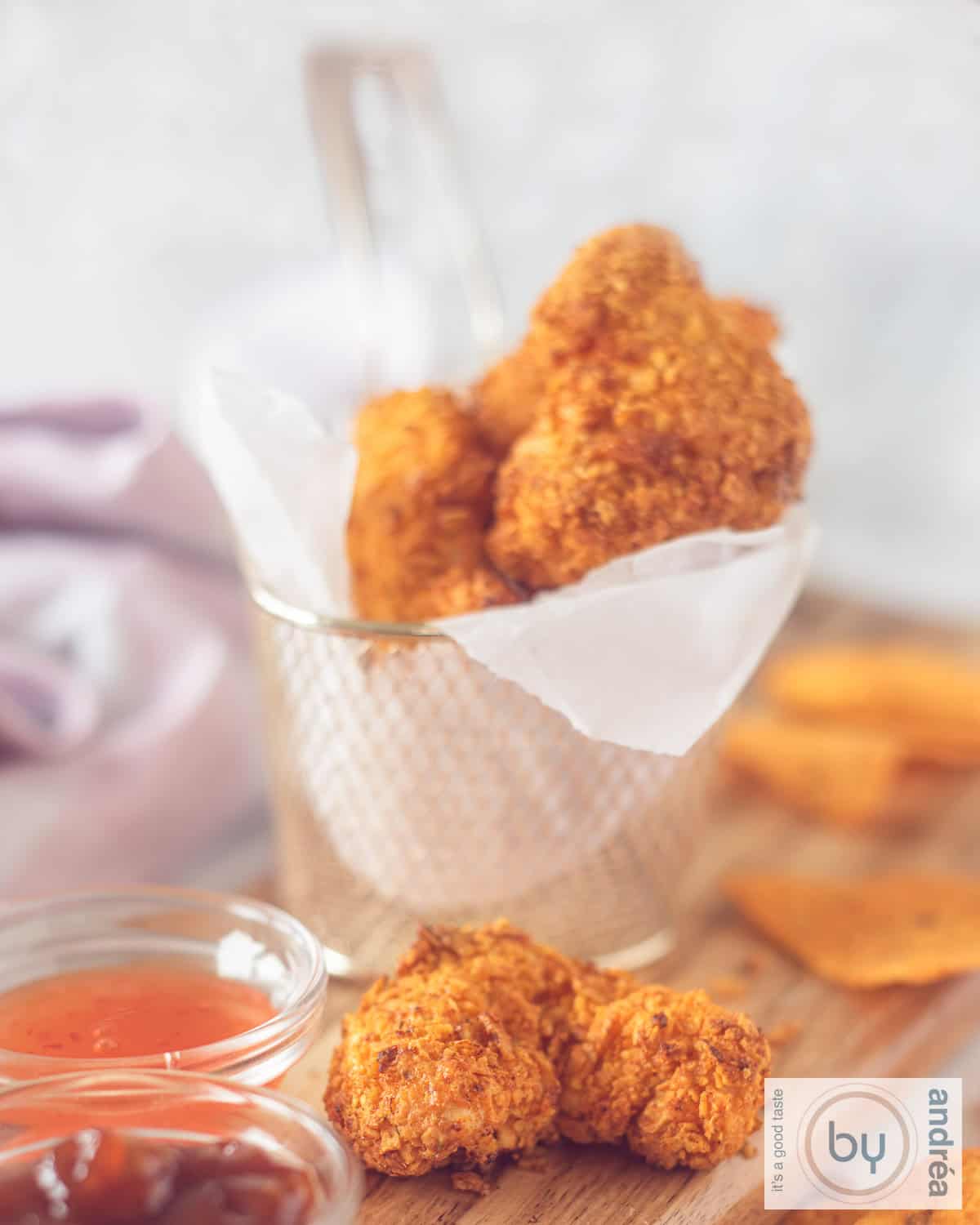 Een foto van een frietmandje met bakpapier gevuld met Dorito kipnuggets, twee liggen ervoor met sausjes en extra chips.