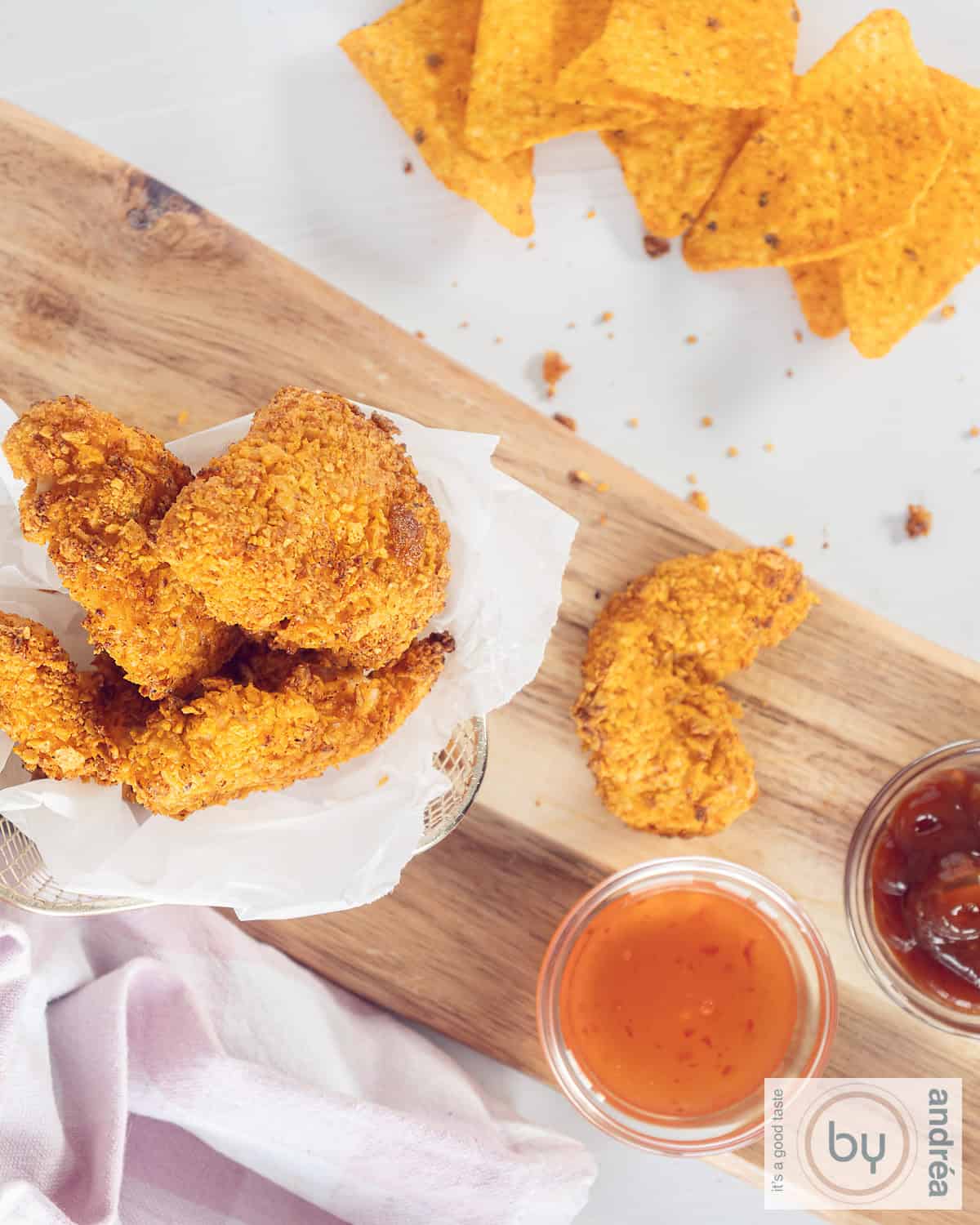 Een foto van bovenaf van een hapjesplank met een kom met Dorito nuggets, twee ervoor en twee sausjes. Bovenin extra Dorito's