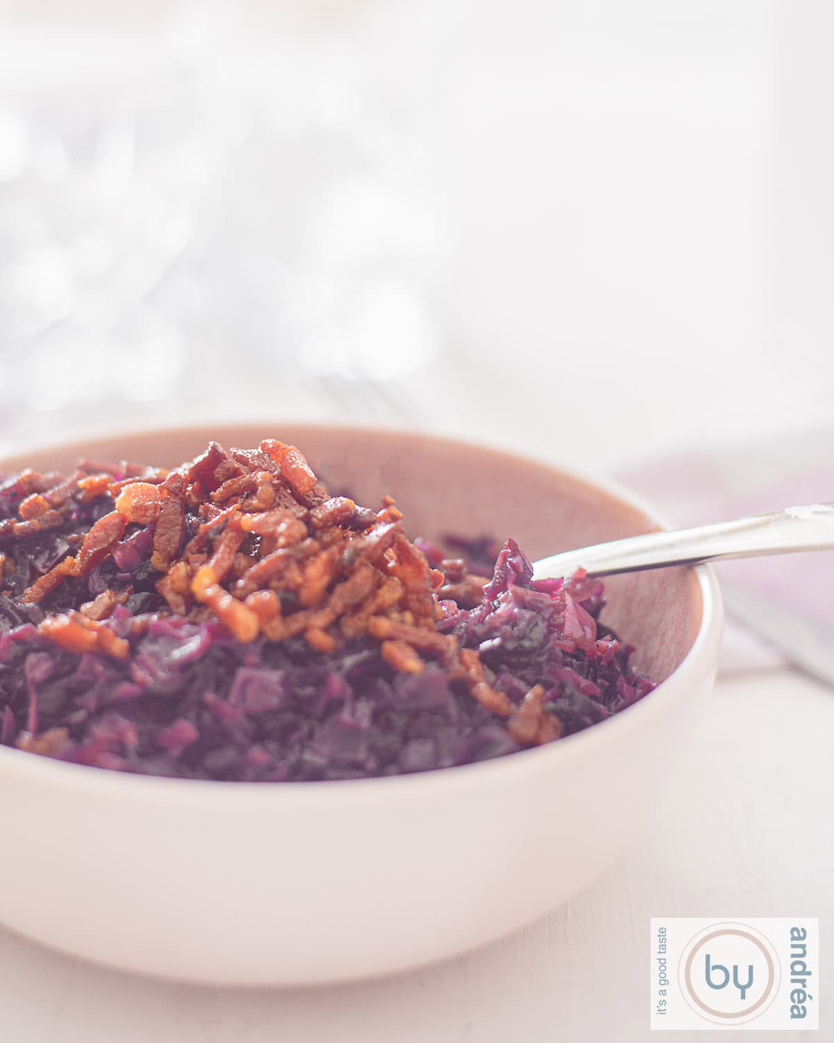 An aerial photo of a pink bowl of red cabbage filled with fried bacon on top, German red cabbage. A white background.