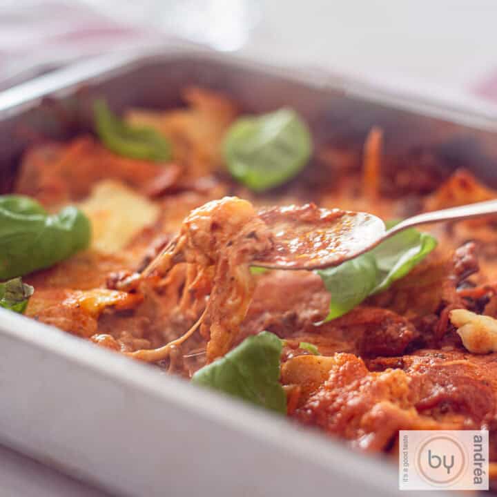 Een vierkante foto van een braadslede gevuld met cheesy eenpans lasagne met mascarpone en gehakt. Een lepel neemt een hap.