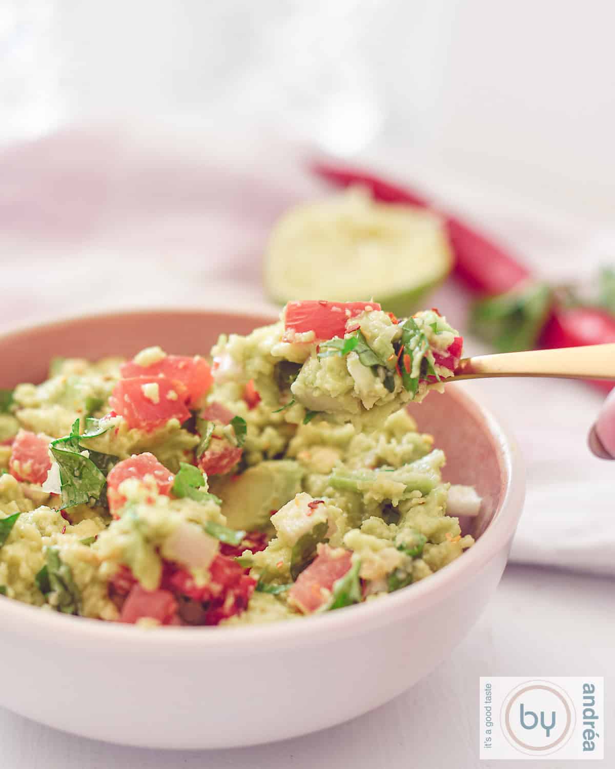 Een hoogtefoto met een roze schaal gevuld met zelfgemaakte guacamole. Een lepel schept een hap eruit.