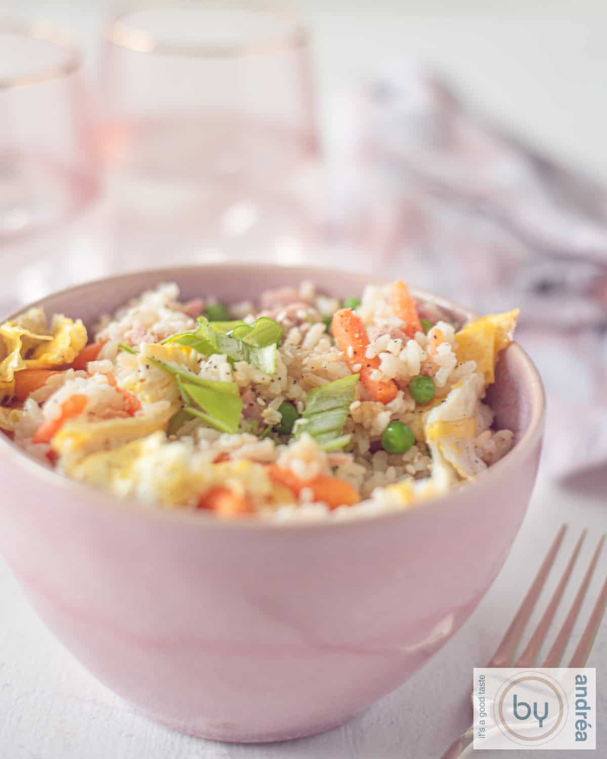 Een hoogtefoto met een bakje met fried rice, groenten, ham en ei. Een roze witte theedoek in de achtergrond
