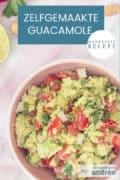Een hoogtefoto met een kom gevuld met guacamole met tomaat, limoen en avocado. Een tekst bovenin: zelfgemaakte guacamole, makkelijk recept