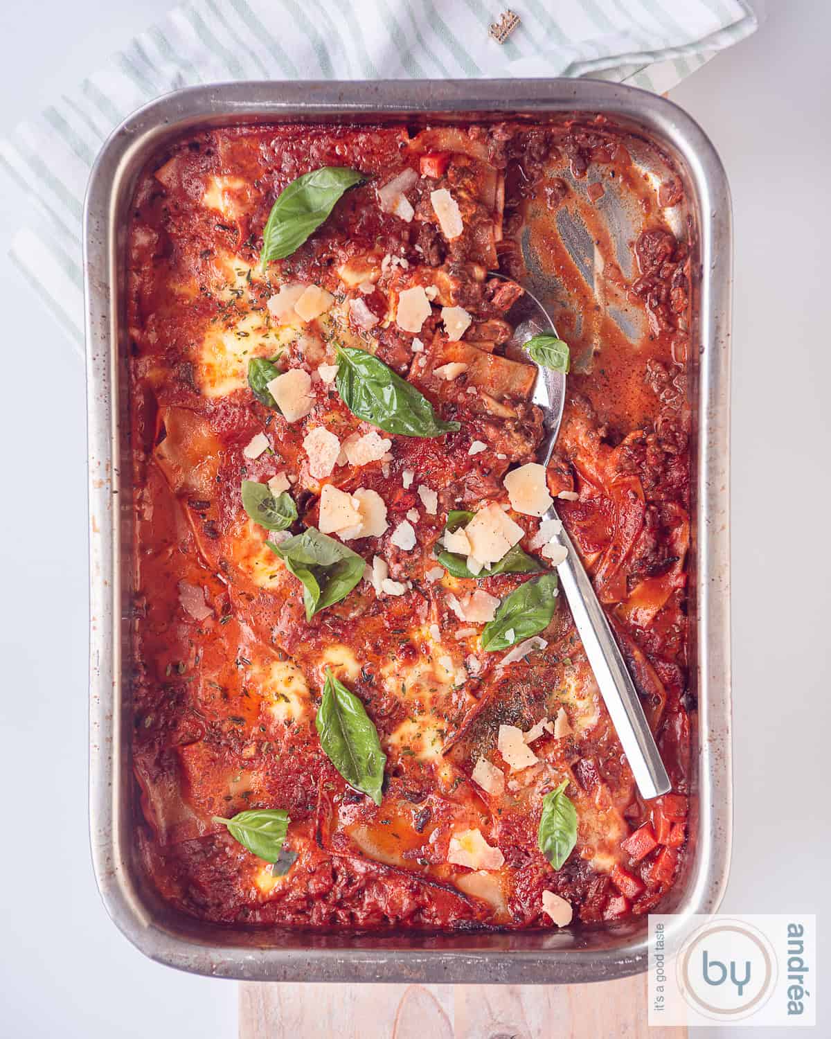 Een foto van bovenaf van een braadslede gevuld met lasagne met bacon, mozzarella, mascarpone en gehakttomatensaus. Een deel is al eruit geschept.