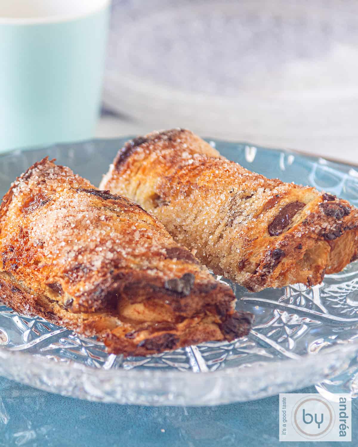 A glass plate with two simple apple rolls on it. A blue mug in the background.