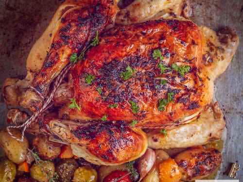 A square photo from above. A chicken on a baking sheet, roasted with, underneath, baby potatoes, vegetables, herbs and garlic.