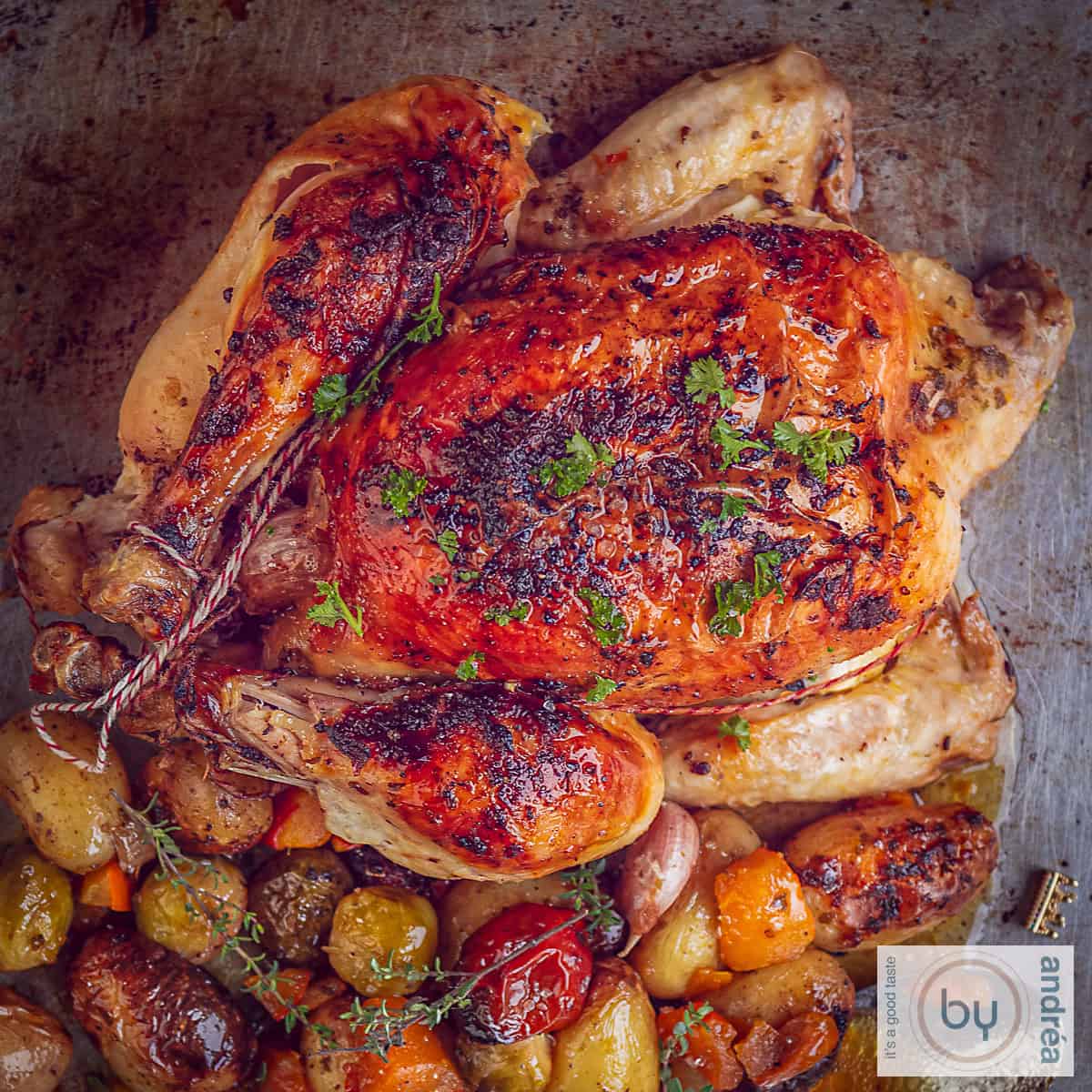 A square photo from above. A chicken on a baking sheet, roasted with, underneath, baby potatoes, vegetables, herbs and garlic.