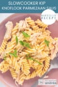 Een roze bord met pasta, kip, saus en petereslie. Een tekst: makkelijk recept, slowcooker kip knoflook parmezaan saus