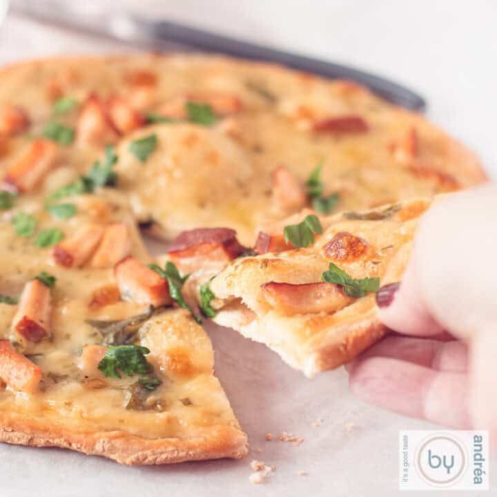 Een vierkante foto met een pizza alfredo waar een hand een punt van pakt.