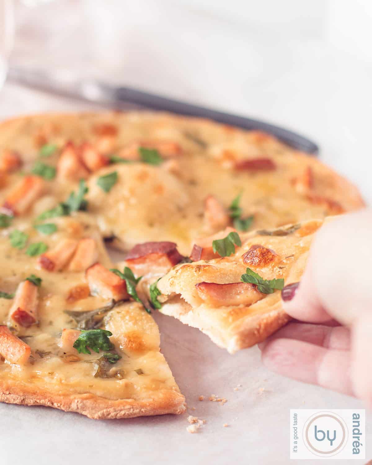 Een hand pakt een pizzapunt van de pizza alfredo op een witte ondergrond.