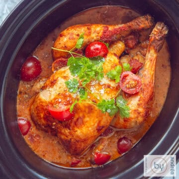 Een vierkante foto van bovenaf met een hele kip in een romige curry kokossaus, cherry tomaten en peterselie.