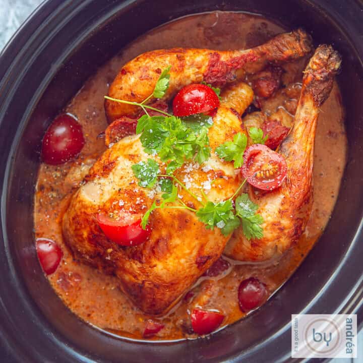 Een vierkante foto van bovenaf met een hele kip in een romige curry kokossaus, cherry tomaten en peterselie.