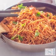 Een vierkante foto met een wok gevuld met Bami Surinaamse stijl met kip en snijselderij.