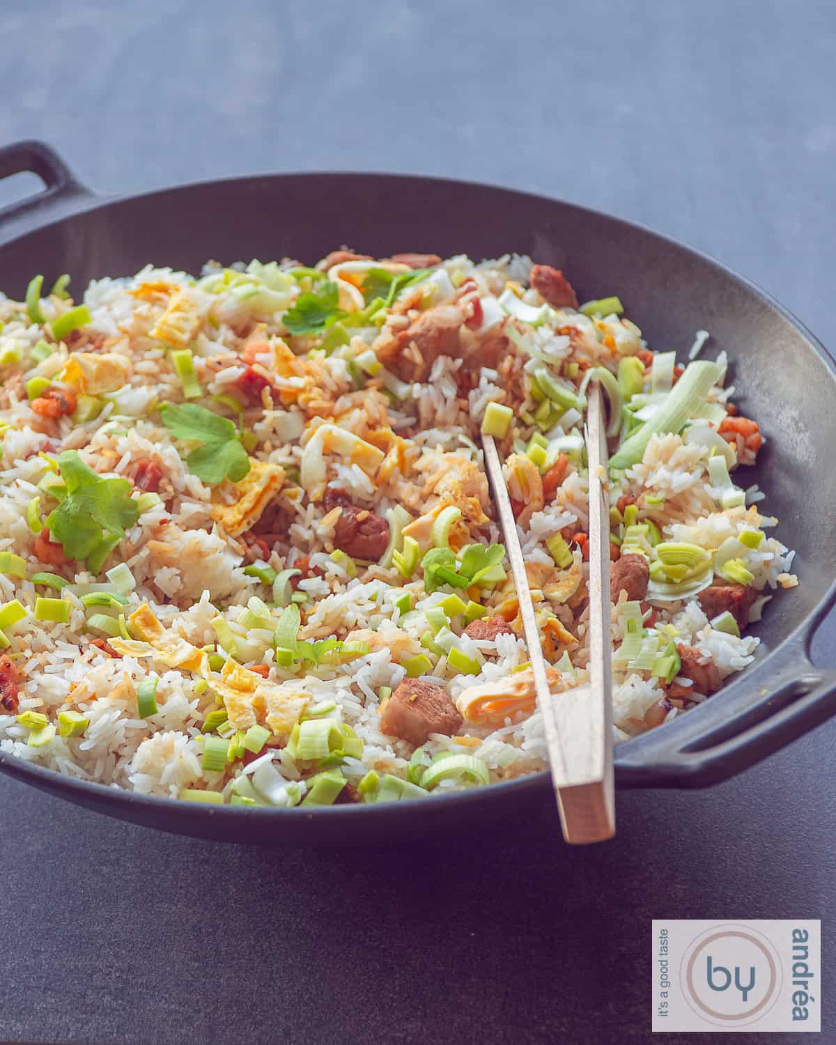 Een hoogtefoto met een wok gevuld met nasi goreng. Een houten knijptang ligt in de wok.