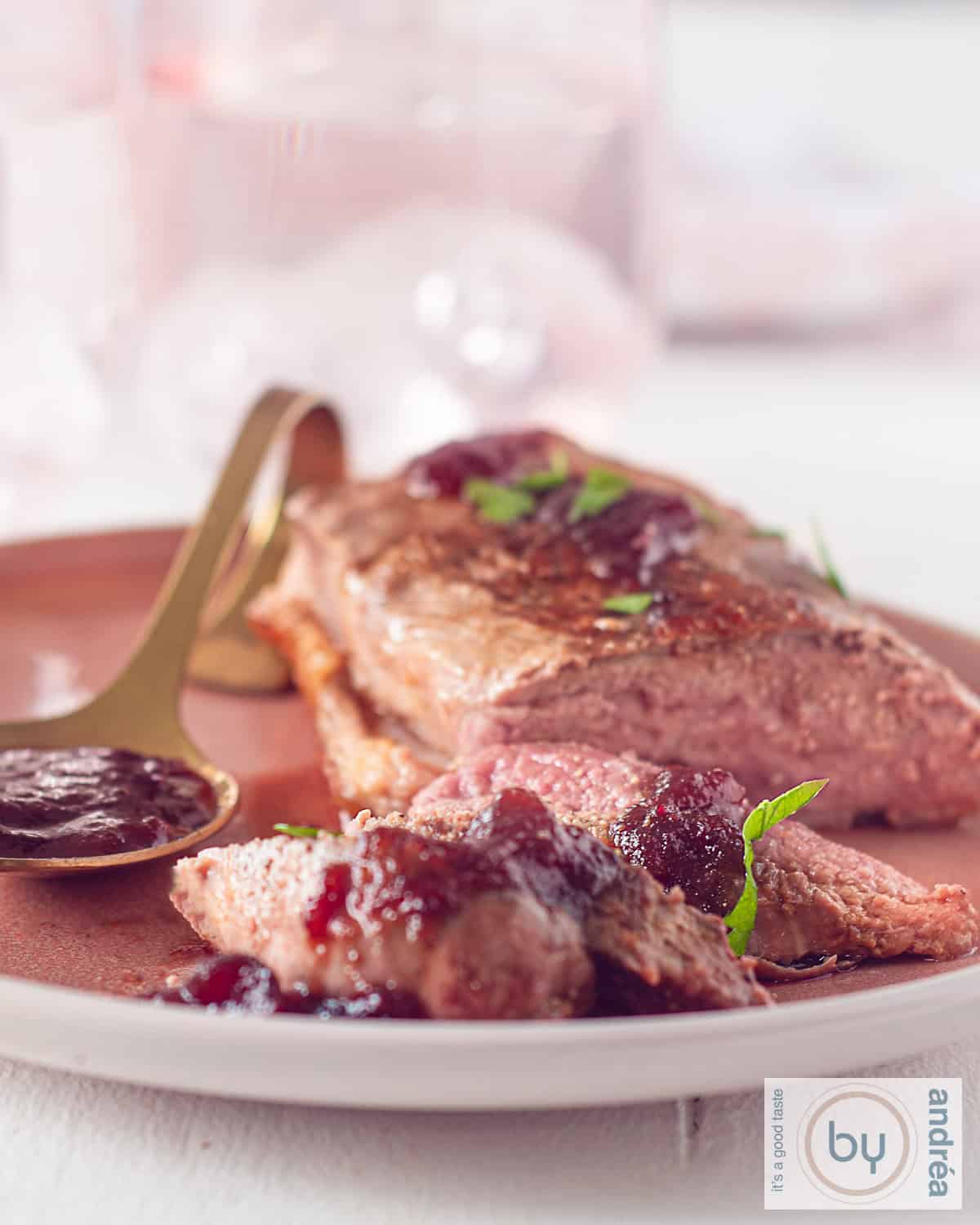 Een roze bord met eendenborstfilet, een paar plakjes afgesneden en zelfgemaakte cranberrysaus.