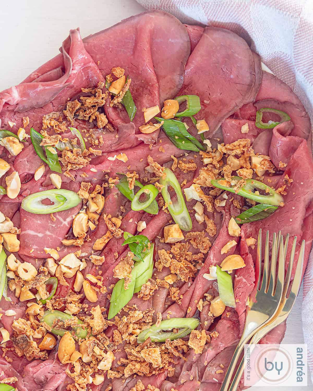Een foto van bovenaf van een schaal met rosbief met garnering en dressing in Aziatische stijl in de vorm van een carpaccio voorgerecht