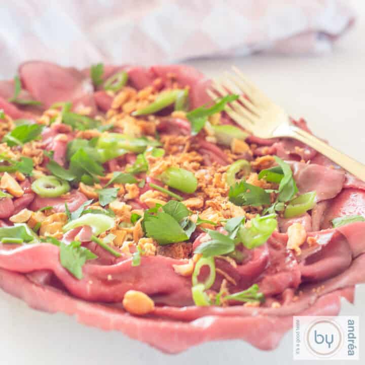 Een vierkante foto met een schaal gevuld met rosbief carpaccio salade Aziatische stijl.