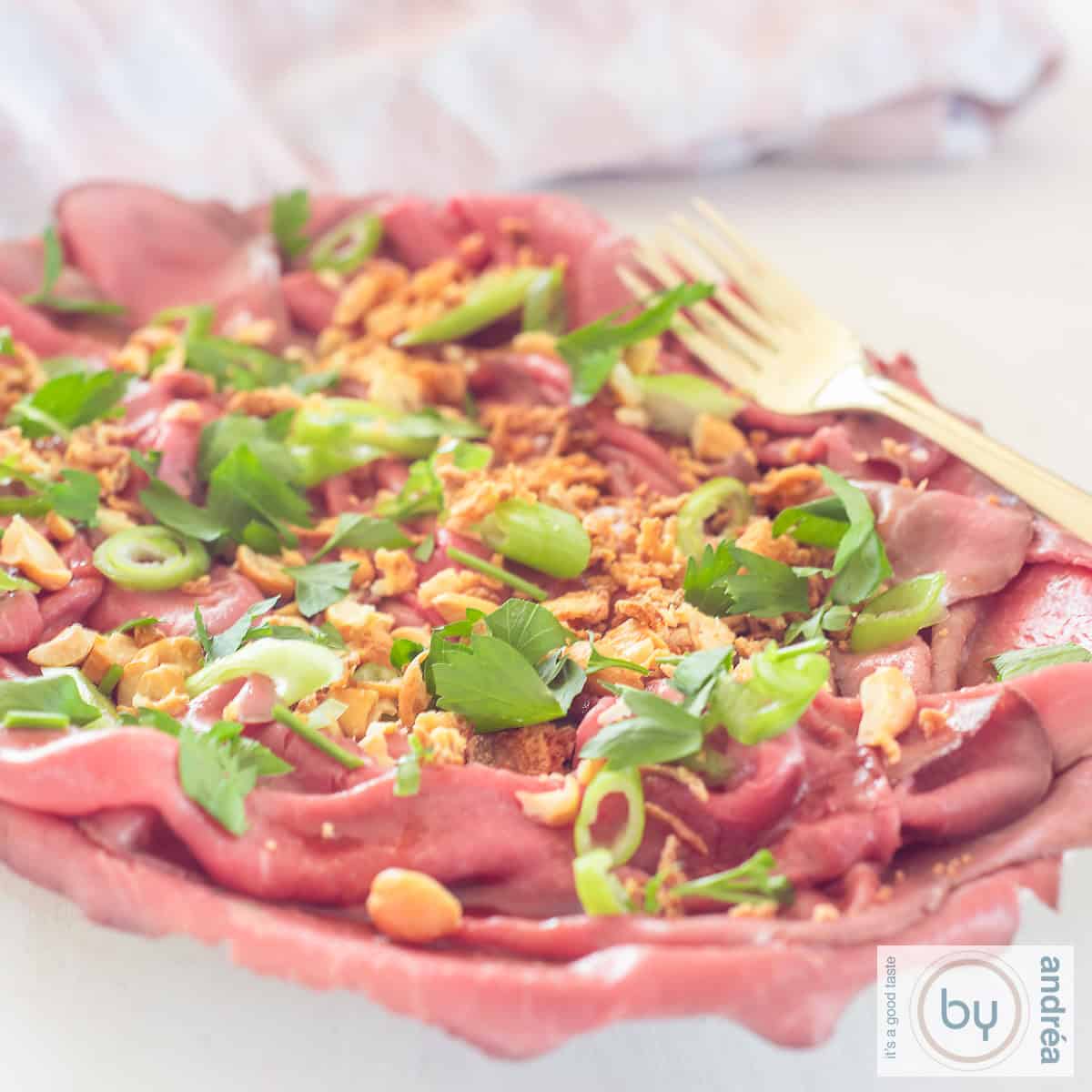 Een vierkante foto met een schaal gevuld met rosbief carpaccio salade Aziatische stijl.