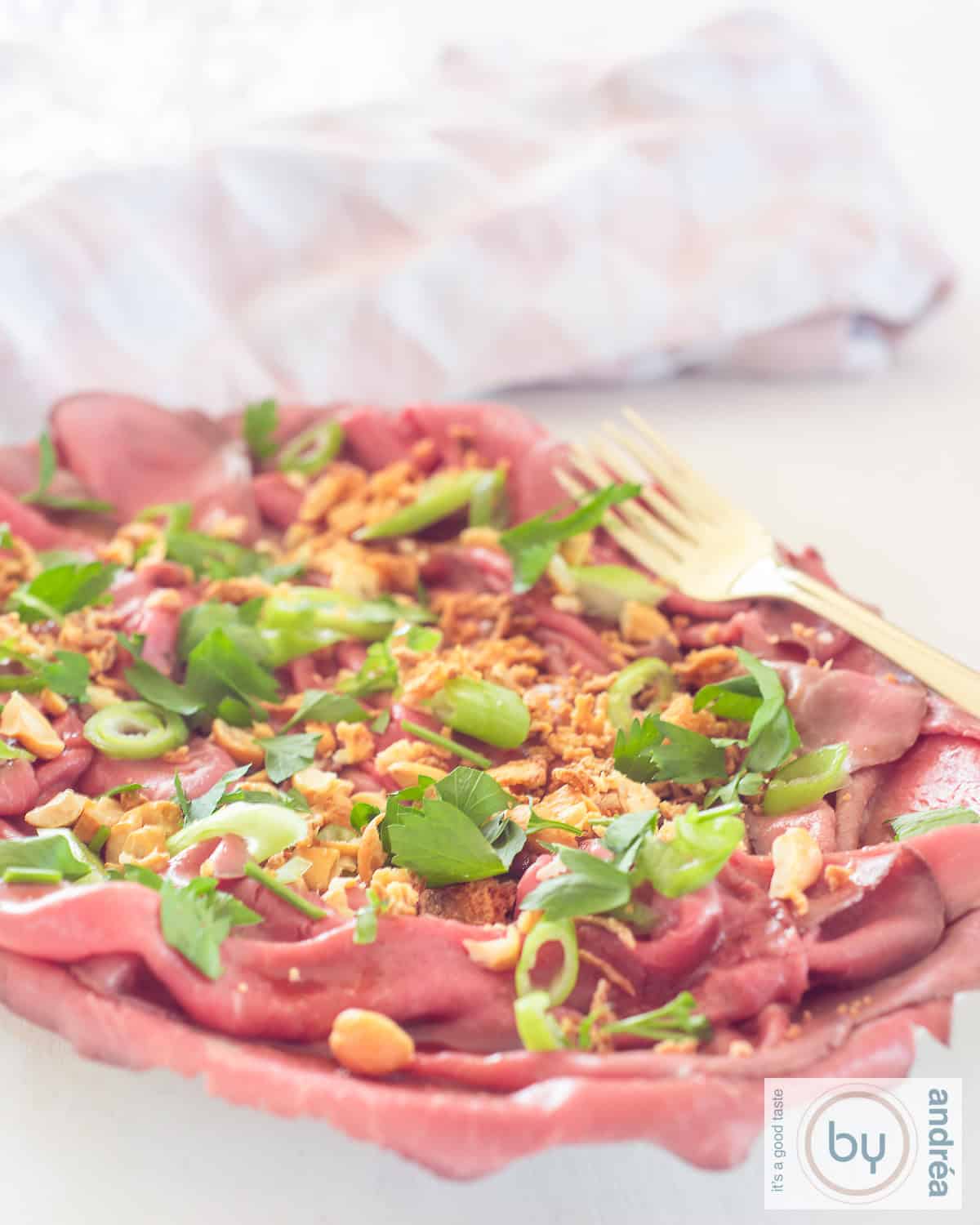 Een hoogtefoto met een schaal met rosbief salade met lente-ui, Aziatische dressing, cashewnoten en uitjes