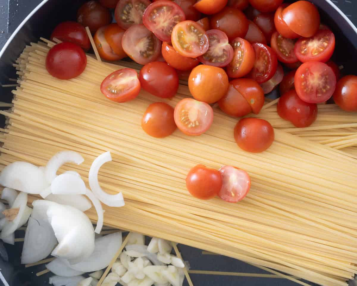 Een hapjespan gevuld met pasta, cherrytomaten, ui en knoflook