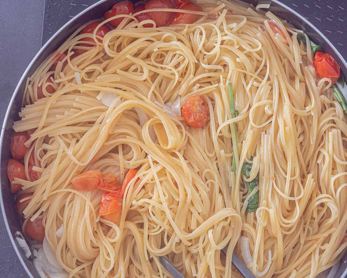 Een hapjespan met gekookte pasta, verse groente en smaakmakers, door elkaar gemixt