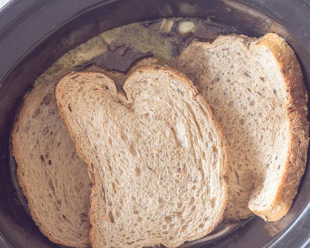 Een slowcooker met inhoud waarop sneetjes brood zijn gelegd.