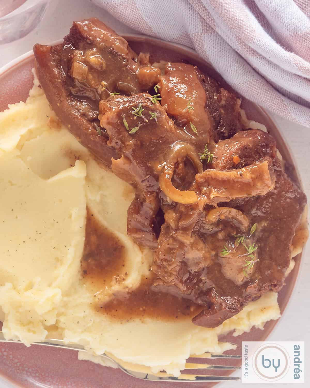 Een foto van bovenaf genomen van een roze bord met sukadelapjes, jus en aardappelpuree