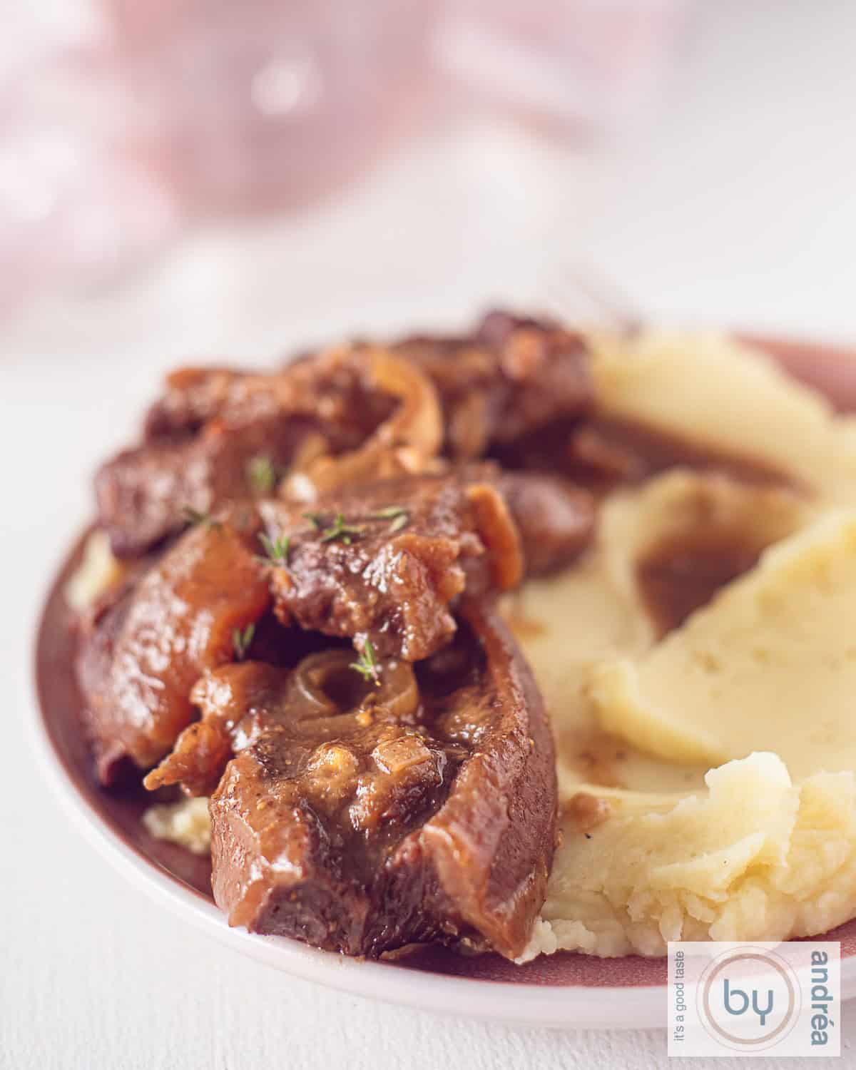 Een hoogtefoto van een deel van een roze bord met aardappelpuree, jus en sukadelapjes.