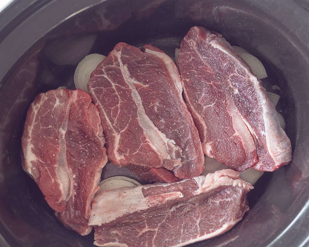 Een laag ui met knoflook en daarop sukadelapjes in de slowcooker