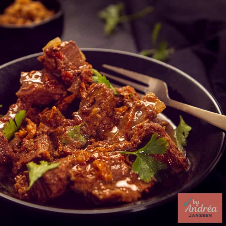 Een vierkante foto met een zwart bord gevuld met zelfgemaakte curry madras uit de slowcooker.